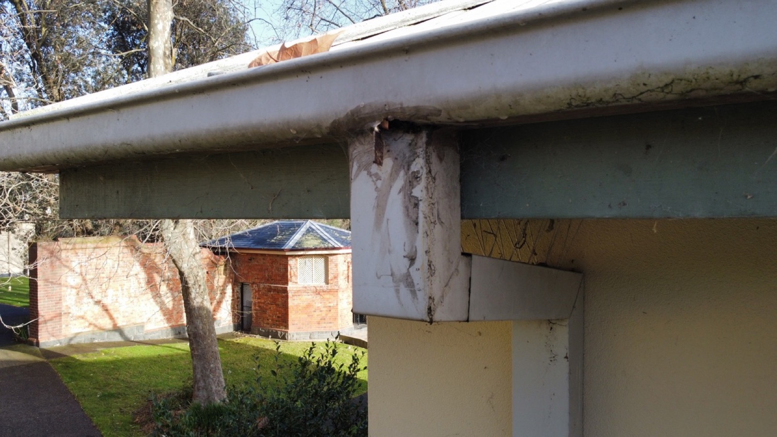 Rusted painted-over eaves gutter with water staining on column — replacement needed
