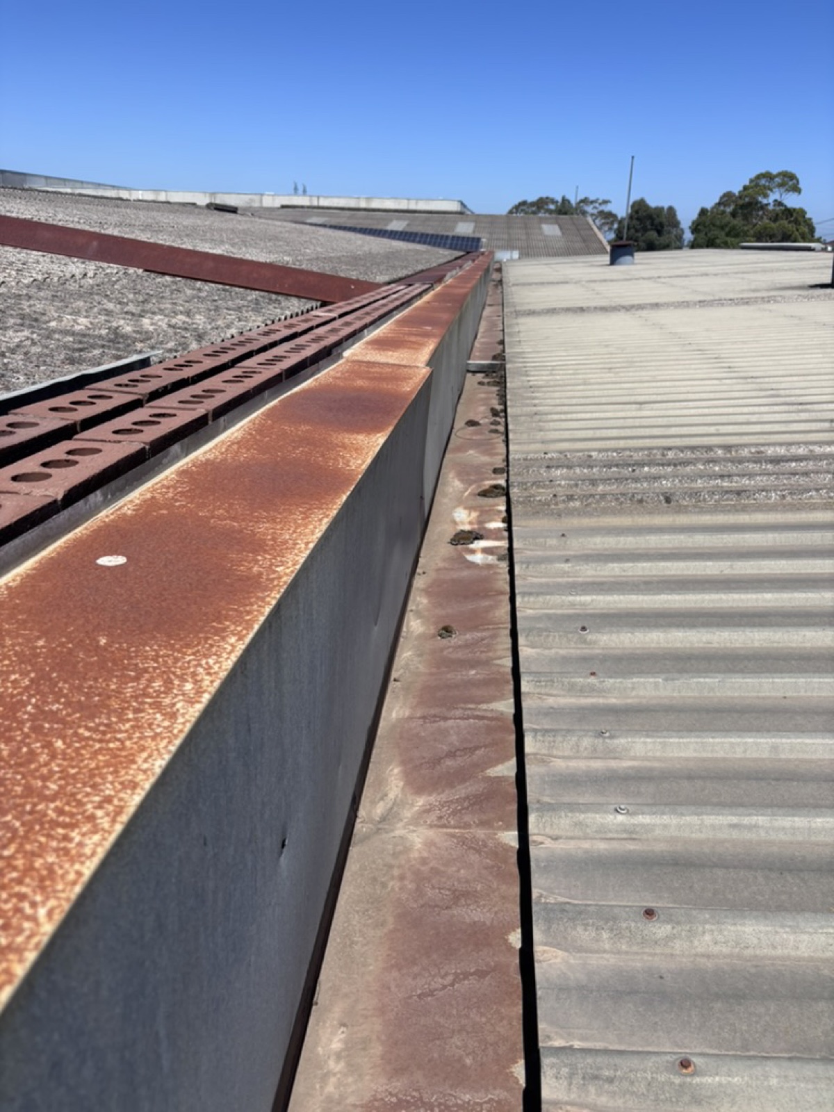 Severely rusted commercial box gutter beside corrugated metal roof — replacement needed